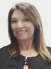 Pessoa adulta com cabelos longos, lisos e castanhos, com mechas mais claras. Tem expressão sorridente, aparência serena e veste blusa preta, com detalhe discreto no decote. O fundo é claro e simples.